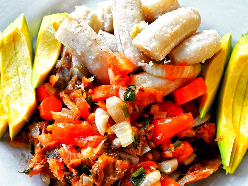 A plate of green fig and saltfish with  avocado sides.